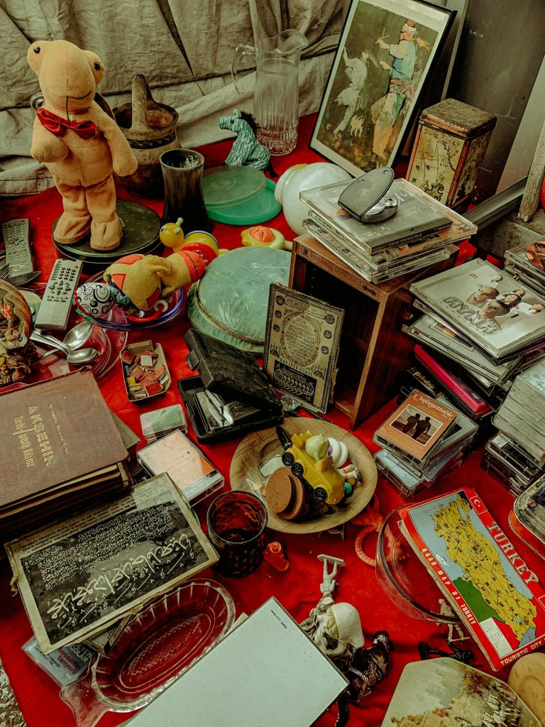 Imagen de antigüedades. Hay libros, cuadros, discos y juguetes en una alfombra roja. Licencia Creative Commons, extraída de Pexels.