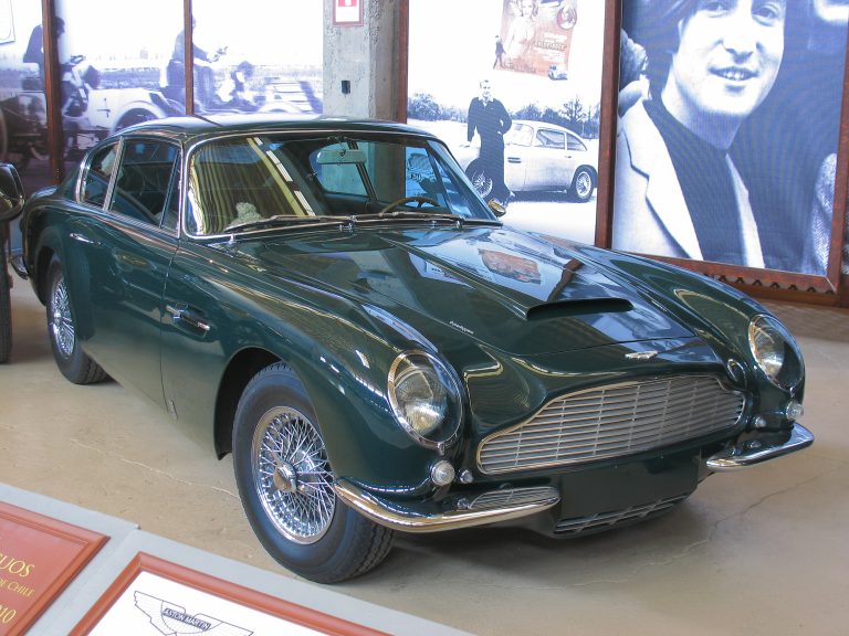 Un Aston Martin DB 6 Vantage Superleggera 1967 de color verde en la exposición del museo frente a unas fotografías. Licencia Creative Commons.