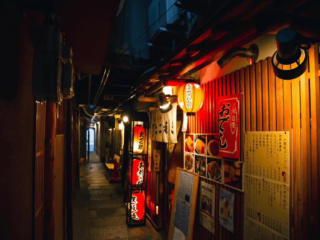 Calle japonesa con lámparas rojas y letreros junto a la entrada a un restaurante.