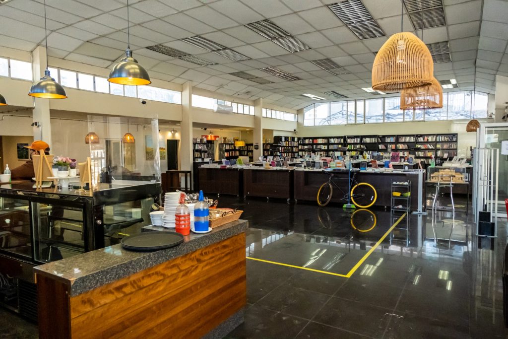 Cafetería en donde se aprecia un poco del bar de atención que mira hacia el fondo del lugar, donde se encuentran altos estantes con libros. 