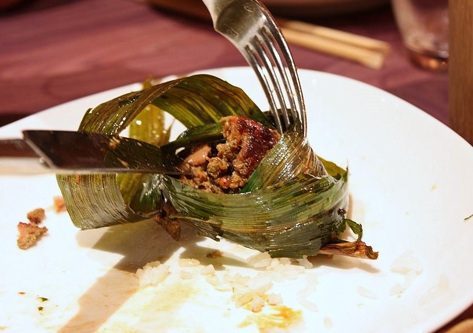 Comida Thai. Es un trozo de carne envuelto en una hoja vegetal encima de una cama de arroz. 