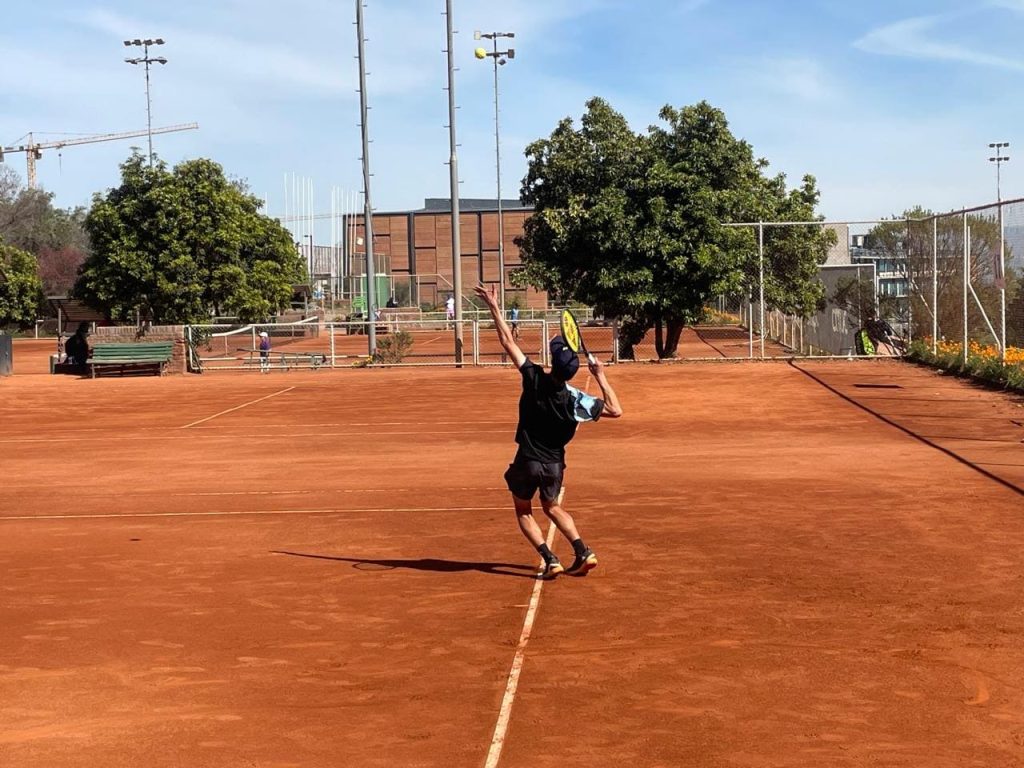 Tenista de la Liga TD realizando un saque de inicio en cancha de arcilla.