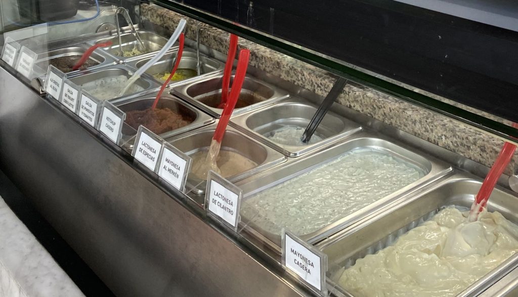 Vitrina de los diversos toppings de local, mayo merkén, mayo casera, lactonesa cilantro y lactonesa de especias entre otras. 
